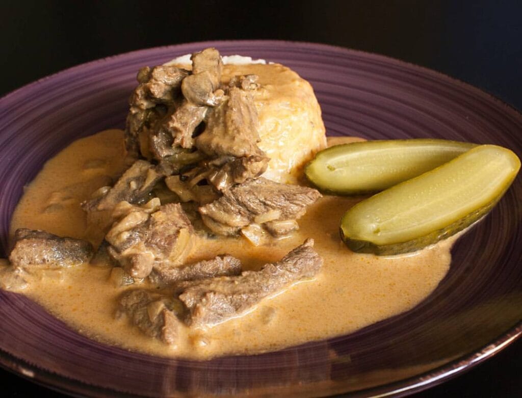 En tallrik med biffstroganoff serverad med saltgurka och ris – klassisk och krämig rätt med smakrik sås