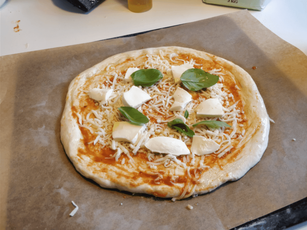 Enkel pizzadeg En pizza innan gräddning, toppad med tomatsås, ost och färska ingredienser, redo för ugnen.