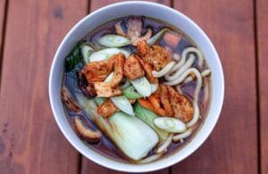 En skål med hemmagjord ramen fylld med nudlar, kokt ägg, vårlök och fläskkarré i en ångande buljong.