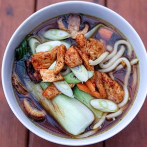 En skål med hemmagjord ramen fylld med nudlar, kokt ägg, vårlök och fläskkarré i en ångande buljong.