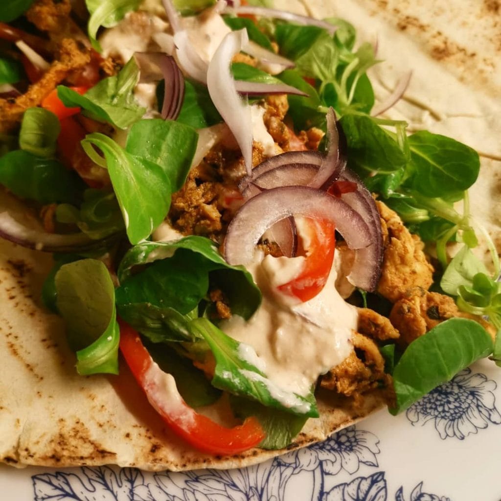 kycklinggyros i ett bröd med sallad vitlöksdressing rödlök tomat på en tallrik