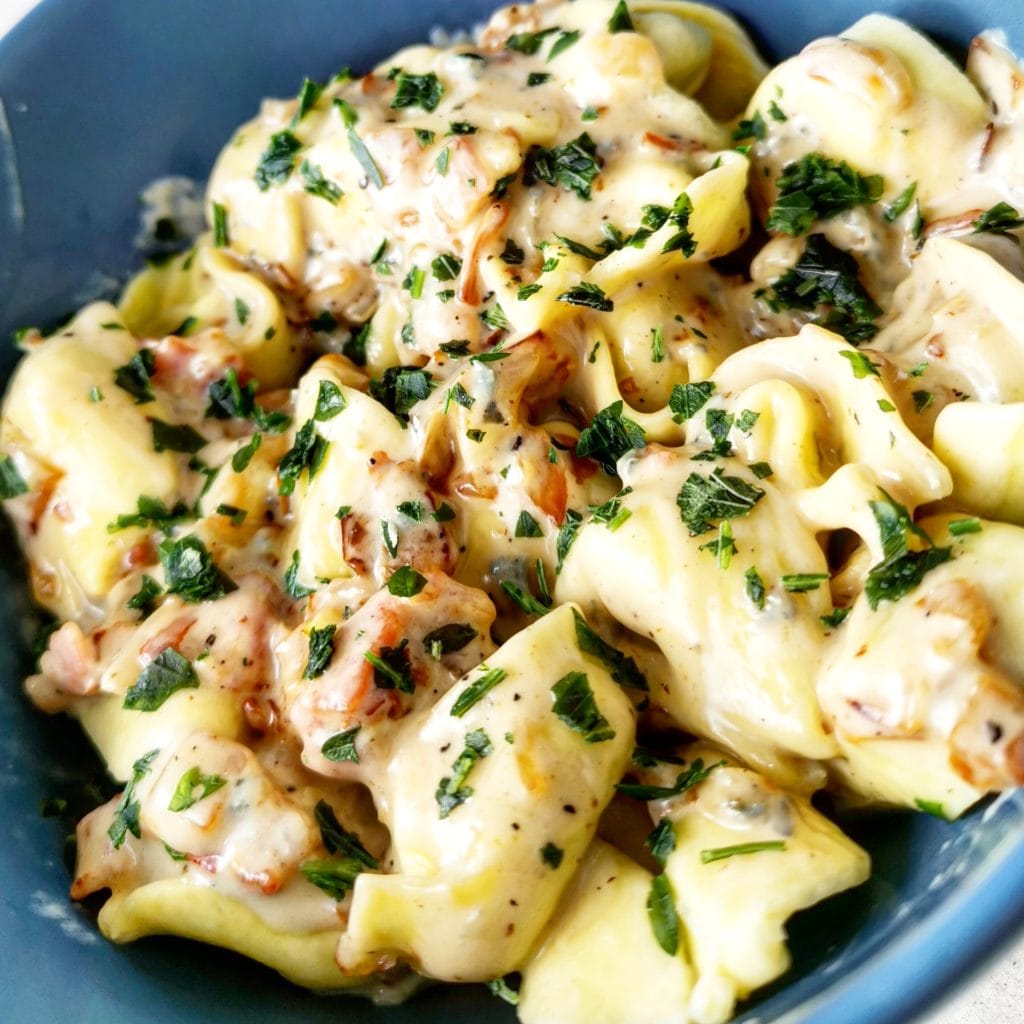 Tortellini med ädelostsås toppad med bacon och persilja