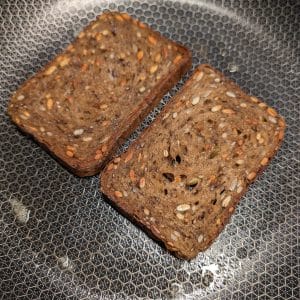 Två brödskivor av rågbröd som steks i en stekpanna med smör
