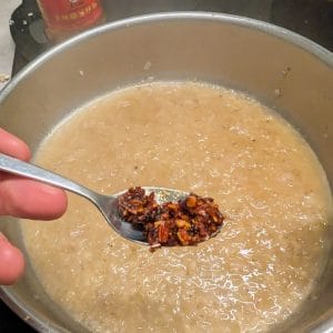Vitt vin schalottenlök och vitlök som kokar samt en sked med krispig chili i olja